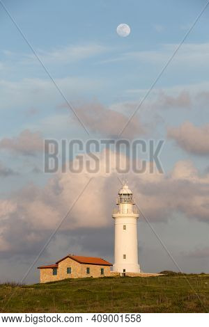 White Lighthouse Against The Background Of The Evening Sunset Sky With Clouds And A Large Moon. Paph