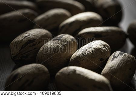A Macro Shot With Selective Focus Of A Handful Of Pecan Nuts In Shells Set On A Wood Table.