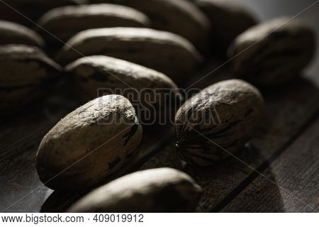 A Macro Shot With Selective Focus Of A Handful Of Pecan Nuts In Shells Set On A Wood Table.