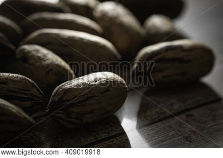 A Macro Shot With Selective Focus Of A Handful Of Pecan Nuts In Shells Set On A Wood Table.