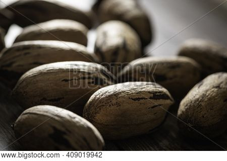 A Macro Shot With Selective Focus Of A Handful Of Pecan Nuts In Shells Set On A Wood Table.
