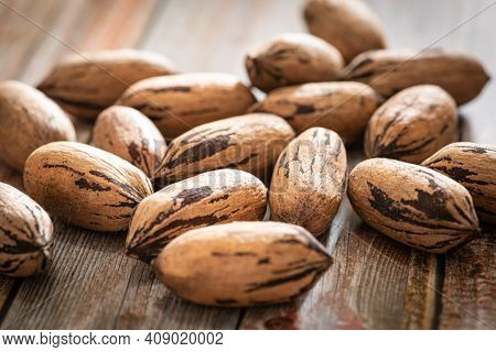 A Macro Shot With Selective Focus Of A Handful Of Pecan Nuts In Shells Set On A Wood Table.