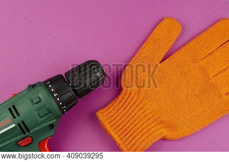 Handheld Power Tools, Repair Services, Or Home Handyman. Electric Drill And Redwork Glove On A Purpl