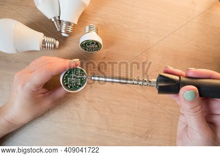 Woman Repairing A Led Lamp With A Soldering Iron.