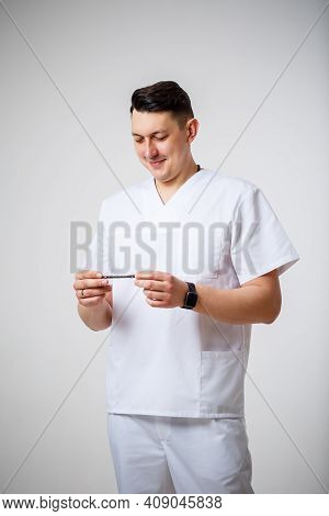 Young Male Doctor In White Surgical Suit Holds And Examines Titanium Plates For Bone Fracture Treatm