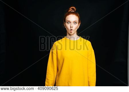 Crazy Joyful Young Woman In Yellow Sweater Fooling Around Making Fish Lips On Isolated Black Backgro