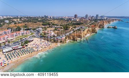 Aerial Drone Shot Of A Busy Beach, Amazing Cliffs, Vegetation And Also Buidlings In The Background. 