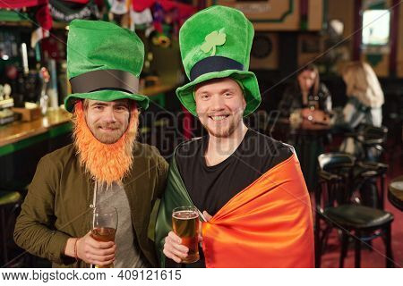 Portrait of two friends smiling at camera drinking beer and celebrating Patricks Day in the bar