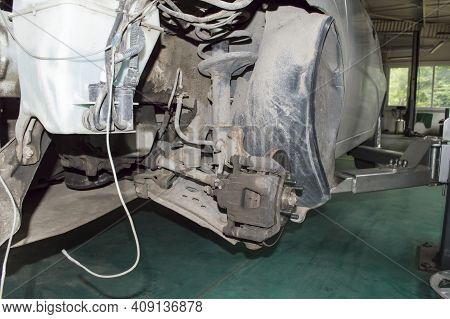 View From The Front Left Wheel Of A Partially Disassembled Gray Car, Which Is Mounted On A Lift In T