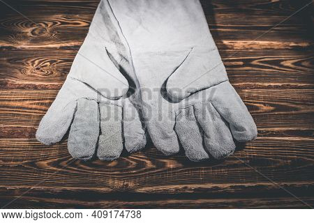 White Leather Welder Gloves On A Wooden Background. A Studio Photo With Hard Lighting.