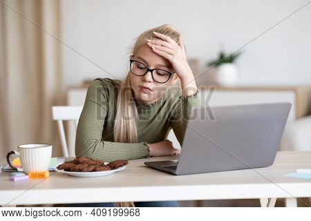 Upset Caucasian Teen Girl Feeling Lonely While Staying Home Alone, Sitting At Table With Laptop, Hav