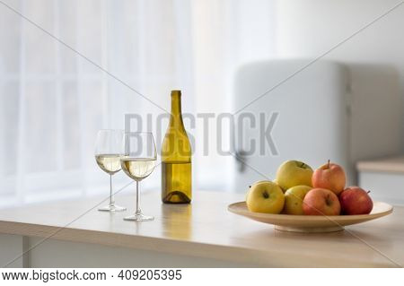 Wine And Fruit For Party And Date In Modern Simple Kitchen Interior. Apples On Plate, Two Glasses An