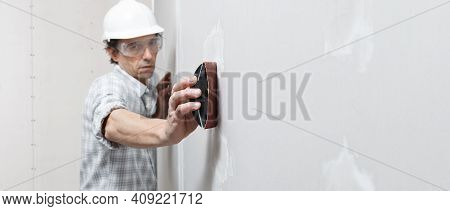 Man Drywall Worker Or Plasterer Sanding And Smoothing A Plasterboard Walls With Stucco Using A Sandp