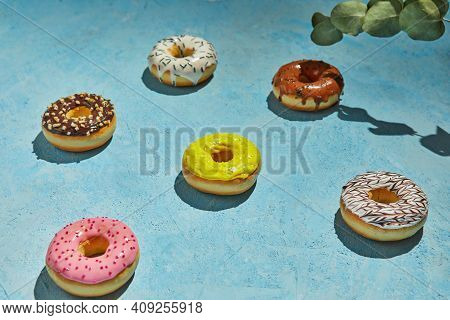 Multicolored Donuts With Frosting, Sprinkles And Leaves On Blue Background