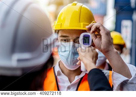 Female Foreman Wearing A Mask Measures The Temperature For A Worker In A Safety Suit. They Stood And