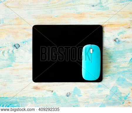 Black pad and blue computer mouse set on wooden colorful background. Modern office mockup for business logo or presentation.