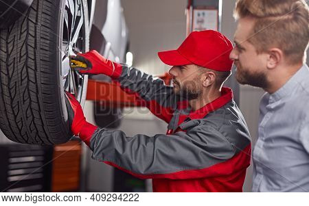 Side View Of Professional Repairman With Wrench Examining Wheel Of Broken Automobile Of Male Client 