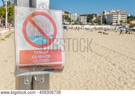 No Bathing Sign From 21:00 To 07:00 In Spanish, Catalan And English. In The Background A Beach On Th