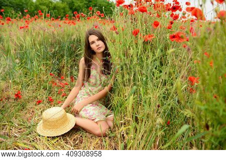 Young beautiful woman rests at poppy field. Attractive girl enjoing life among blooming red flowers, summer nature outdoor 