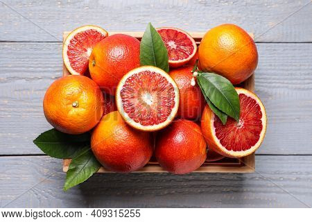 Crate Of Ripe Red Oranges And Green Leaves On Grey Wooden Table, Top View