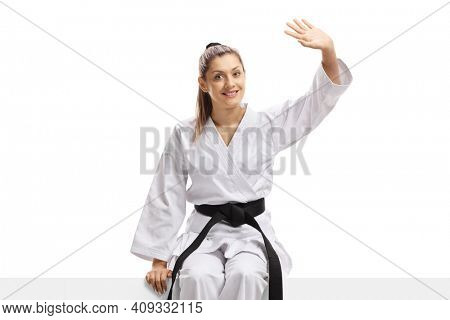 Woman in karate kimono sitting on a panel and waving isolated on white background