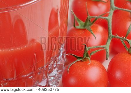 Half Full Glass With Tomato Juice With Pulp Stands On A Table Next To Tomatoes On A Branch Close-up 