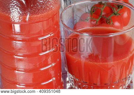 Half Full Glass With Tomato Juice With Pulp Stands On A Table Next To Tomatoes On A Branch Close-up 