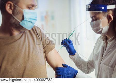 Young Woman Nurse With Surgical Mask And Face Shild Giving Injection To Senior Man. Covid-19 Or Coro