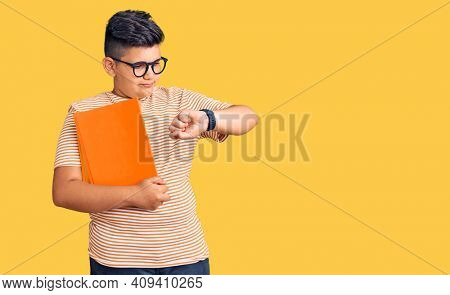 Little boy kid holding book wearing glasses checking the time on wrist watch, relaxed and confident 