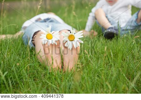 Boy Lying On Green Grass Outdoors In Park. Happy Summer Feet. Child With Daisy Lying In Sunny Meadow