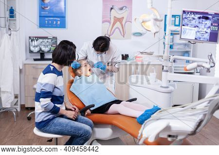 Kid Patient In Dentistiry Office Getting Treatment For Teeth Cavity Sitting On Dental Chair Wearing 