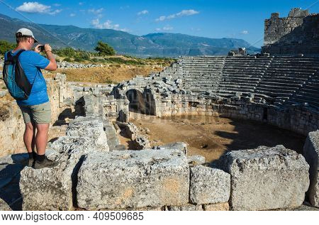 Man tourist standing on ruins of Theatre in Xanthos Ancient Lycia City and taking photo, Turkey. Sunny day, Old Lycian civilization heritage architecture amphitheater
