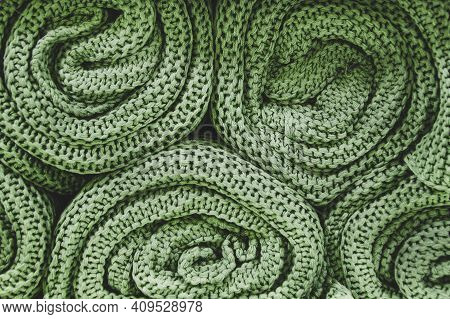 Green Knitted Blankets Rolled Into Rolls. Knitted Texture, Factory Textiles. Neat Pile Of Rolled Kni