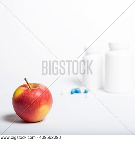 Red Apple Closew Up And Blue And White Pills From Conteiners On A White Background.