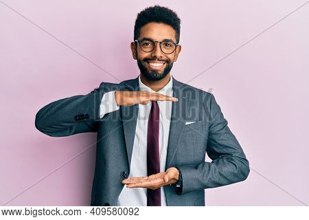 Handsome hispanic business man with beard wearing business suit and tie gesturing with hands showing big and large size sign, measure symbol. smiling looking at the camera. measuring concept. 