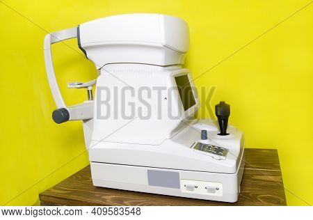 A White Autorefractometer Against A Yellow Wall, A Device Used In Ophthalmology And Optometry To Ass