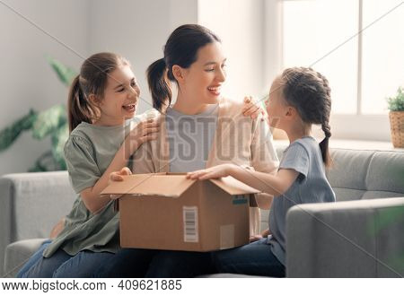 Mother and daughters are unpacking cardboard box at home.