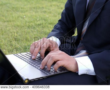 Businessman Sits Outside In The Park And Works With His Laptop