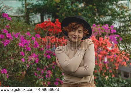 A Beautiful Plus Size Girl In A Hat Smiles Among The Green Plants Of Greenhouse