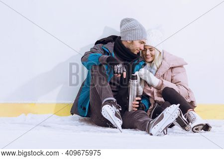 Young Caucasian Couple In Love In Winter With Ice Skates Posing Together With Vacuum Flask In Snowy 