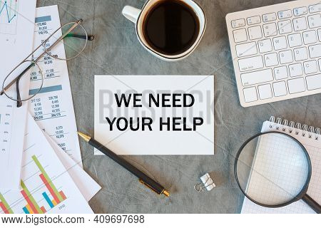 We Need Your Help Is Written In A Document On The Office Desk With Office Accessories, Coffee, Diagr