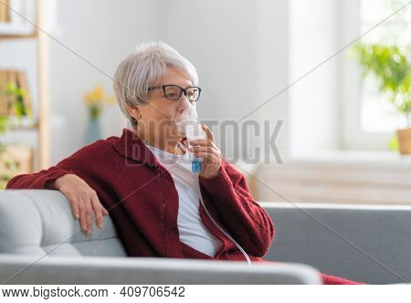 Elderly woman using inhaler for asthma and respiratory diseases at home.