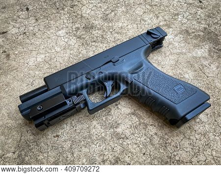 Bangkok Thailand - 21 February 2021: Air Soft Gun Glock 18C Pistol Gun With Laser Sight On The Floor