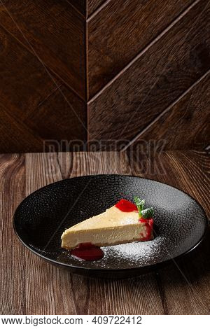A Piece Of Cheesecake Served With Red Berry Sauce, Mint Leaf And Sugar Powder. Isolated Dish In A Bl