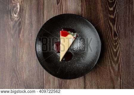 A Piece Of Cheesecake Served With Red Berry Sauce, Mint Leaf And Sugar Powder. Isolated Dish In A Bl