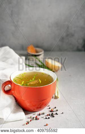 Hot Homemade Beef Bone Broth With Collagen And Amino Acids In Red Bowl With Red Napkin And Green Oni