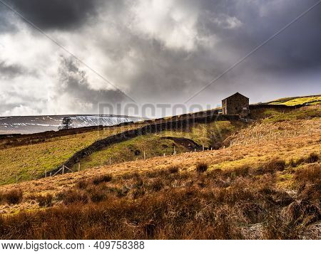 An Old Ruined Barn On A Hill, With Dry Stone Walls And Open Moorland With Snowy Mountains In The Dis
