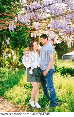 Family Of Three Under A Blooming Wysteria Tree On A Sunny Day