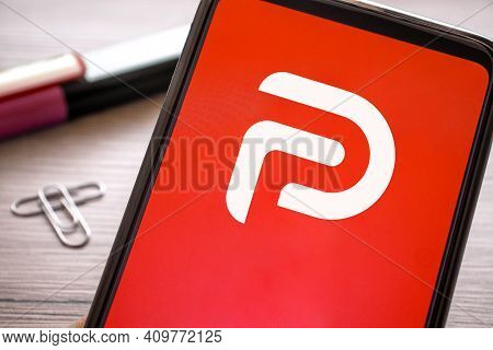 Smartphone With Red Parler Logo On Wooden Table. Phone Concept Social Media Platform Icon Display On