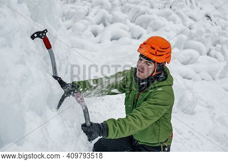 Alpinist Man With Ice Tools Axe In Orange Helmet Climbing A Large Wall Of Ice. Outdoor Sports Portra